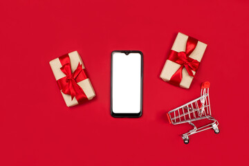 Smartphone mockup. Gifts, smartphone, shopping cart flat lay on red background top view, copy space. Onile christmas shopping concept. 2021 Happy new year, xmas holidays. Advertising, marketing