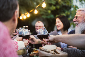 Happy family dining and tasting red wine glasses in barbecue dinner party - People with different ages and ethnicity having fun together