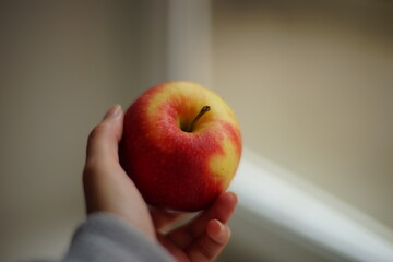 Ripe red apple in female hnd near the window