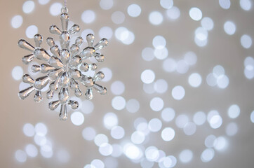 Transparent toy snowflake. Bokeh. Silver Christmas lights.
