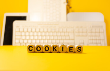 The word cookies written with real wooden dices in front of a yellow background with computers and keyboard © valentine