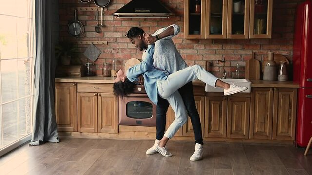Full length view young African stylish 35s couple, active boyfriend girlfriend in love dancing tango perform passionate and sensual movements in home kitchen. New house, relocation celebration concept
