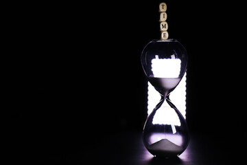 Sand running through the bulbs of an hourglass measuring the passing time in a countdown to a...