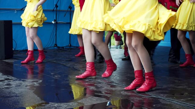 Feet of girls in yellow dresses and boots dancing on the wet street stage. Fairy in russian village