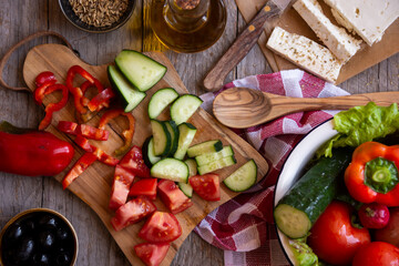 Fototapeta premium Ingredients for a vegetable salad - tomatoes, cucumber, feta cheese, cut vegetables. Preparing Greek salad