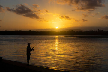 Silhouette of a man fishing in the bay at sunset.