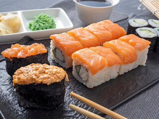 a variety of rolls and sushi gunkan nested on a black plate. next to it are bamboo wasabi sticks and sauce. Side view. traditional Japanese cuisine