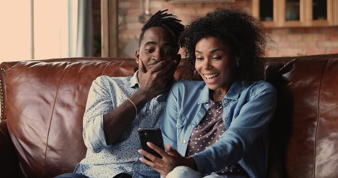 African sport fan couple sit on couch at home watching game match on-line in streaming on smart phone celebrating victory. Happy supporters cheering and exulting after winning on internet bet concept