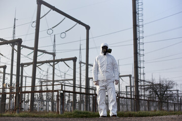 Full length of male worker standing on territory of power station with high voltage electricity...