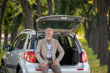 Senior man sitting on trunk of the car