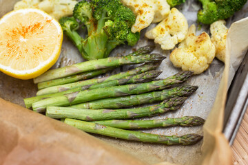 Baked asparagus, broccoli and cauliflower with spices and lemon on parchment paper close up. Vegan healthy diet food concept