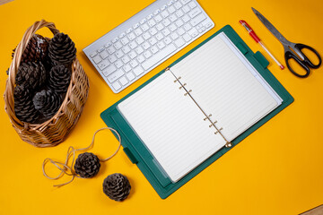 open notebook journal with Christmas cones in a wicker basket yellow background