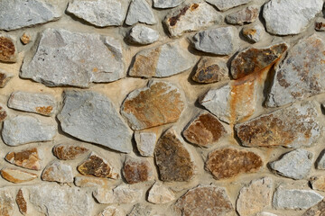 Background of flat stones and cement, decorative wall made of natural materials. Stony hard surface made of parts of different sizes and shapes with a sandy tint