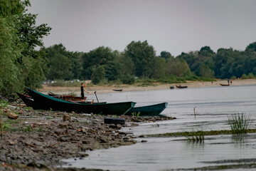 Old boats made of wood and metal on the river Bank among rocks and vegetation. Parked water transport in nature. Simple landscape.