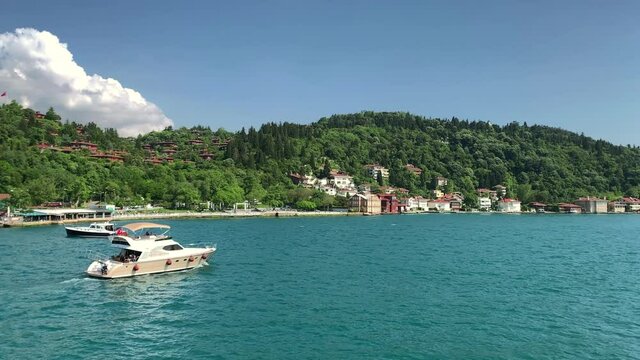 Footage of a luxury yacht passing on Bosphorus by upscale neighborhood called "Kandilli" in Istanbul. It is a beautiful scene in a sunny summer day. Camera moves forward.