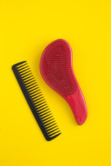 Top view of black and red hair combs on the yellow background. Location vertical.