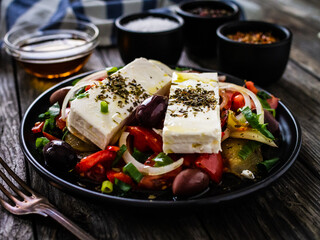 Fresh Greek salad - feta cheese, tomatoes, cucumber, red pepper, black olives and onion on wooden table
