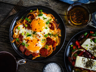 Continental breakfast - sunny side up eggs  on sausages, onion and greek salad on wooden table
