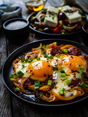 Continental breakfast - sunny side up eggs  on sausages, onion and greek salad on wooden table

