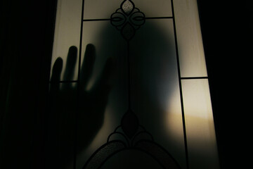 A silhouette man standing behind the door,hand on the window, Thriller concept, Blurred edit