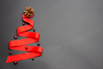 The red ribbon Christmas tree is decorated with a cone and berries on a black background. The concept of the Christmas tree.