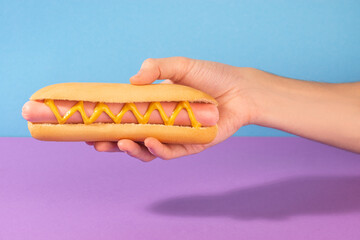 Hand giving a fresh hotdog with mustard zigzag