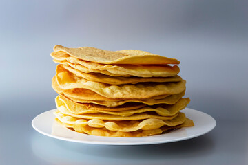 Yellow, flat, thin, baked cakes on a white plate. Light gray background.