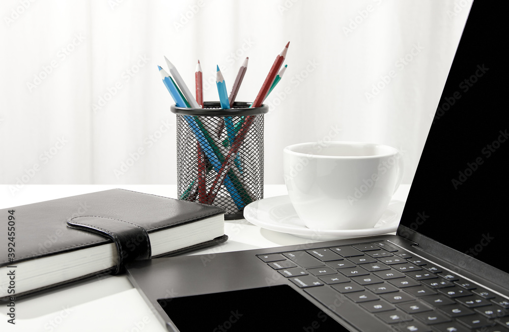 Sticker Closeup of a laptop, a cup of coffee, a notebook and pencil holder on a white desk, indoors