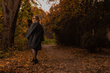 A young girl in a black cloak stands in chameleon glasses in autumn. Yellow forest, green grass, blonde. with charismatic appearance enjoy the concept