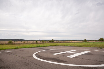 Fototapeta premium Private helipad after rain. An asphalt helipad against the backdrop of a green field and a cloudy evening sky.