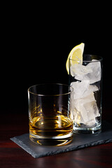 Whiskey neat and glass of ice served on slate plate. Dark red wooden table, high resolution