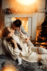 Wonderful couple sit near the fireplace at home, loving husband gently kiss lovely wife, enjoy tender moments, cozy winter holidays, Christmas celebration concept