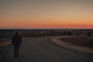 Fototapeta na wymiar Man walks along turning paved road on hill at sunset. Copy space
