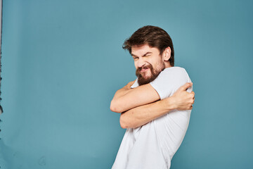 A bearded man in a white T-shirt gestures with his hands emotions blue background