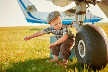 Funny little boy traveler sits near the landing gear of the plane and waits for the flight