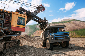 Excavation work in mountainous areas - mining. The excavator loads the mountain soil with a bucket into the body of a mining dump truck. © Letopisec