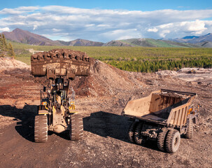     Dump truck and wheel loader in operation. Mining.   A wheel loader loads mountain soil into the body of a dump truck.  © Letopisec