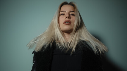 Alluring young sexy and beautiful blonde woman looking at camera giving attractive poses in cyan-color studio background, lifestyle, fashion and photography concept