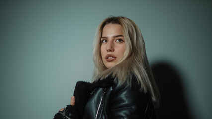 Fototapeta premium Alluring young sexy and beautiful blonde woman looking at camera giving attractive poses in cyan-color studio background, lifestyle, fashion and photography concept