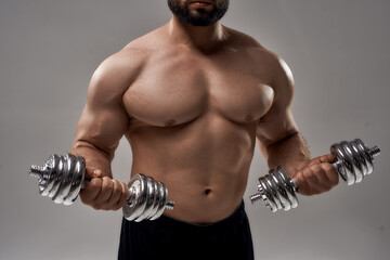 Fototapeta na wymiar Figure of young muscular caucasian sportsman lifting dumbbells