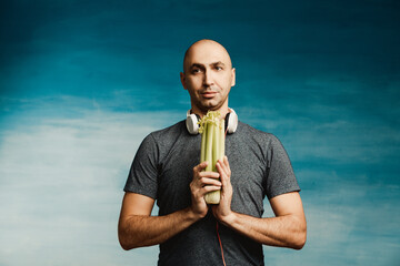 Funny bald man in headphones holds a celery on a blue background.