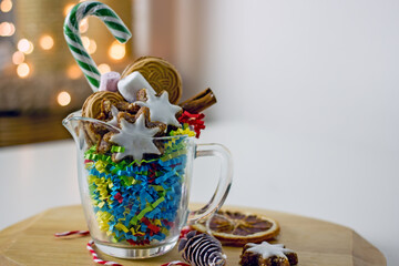 Christmas homemade sweet gifts. Christmas composition of transparent mug with cookies. Handmade home gift idea mugs with sweets, cookies, nuts, lollipops cane and New Year decorations on a light table