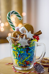 Christmas homemade sweet gifts. Christmas composition of transparent mug with cookies. Handmade home gift idea mugs with sweets, cookies, nuts, lollipops cane and New Year decorations on a light table
