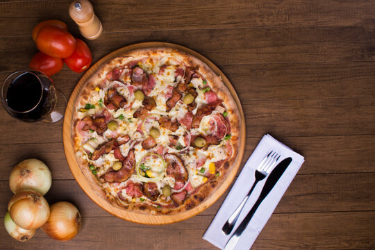 Delicious Portuguese Pizza made with ham, pea egg, heart of palm, pepperoni, onion and mozzarella and bacon. Served on wooden board. Top close-up photograph. Glass of red wine. Space for text.