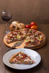 Portuguese pizza made with ham, pea egg, heart of palm, pepperoni, onion and mozzarella and bacon. Vertical gastronomic photography. Pizza slice served. Red wine to accompany.