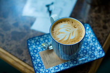 Blue striped ceramic cup with latte on a rectangular saucer with blue pattern close up