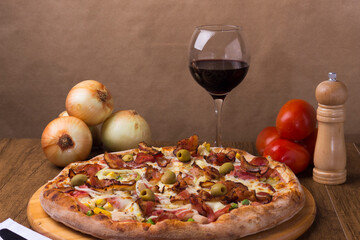 Portuguese pizza made with ham, pea egg, heart of palm, pepperoni, onion and mozzarella and bacon. Served on a wooden board with red wine to accompany the food. Centralized elements.