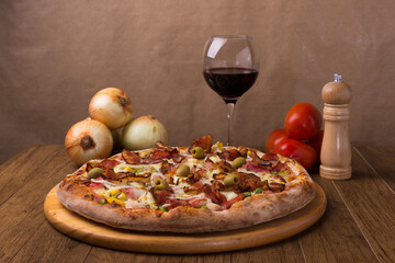 Delicious Portuguese Pizza with a glass of red wine. Gastronomic photograph with rustic onions and tomatoes in the background.