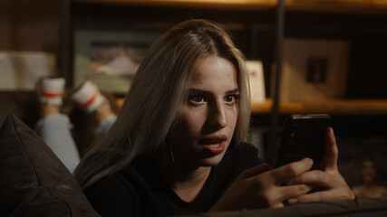 Young beautiful sweet blonde woman lying on sofa and chatting with her phone in hand, lifestyle and social media concept