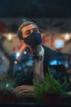 Portrait of young handsome African American man wearing protective face mask waiting for his order photographed through the window of a street cafe or restaurant (selective focus)